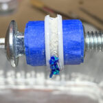 screw wrapped in blue tape with iridescent pieces