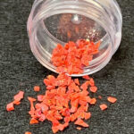 Red plastic flakes spilling from clear jar