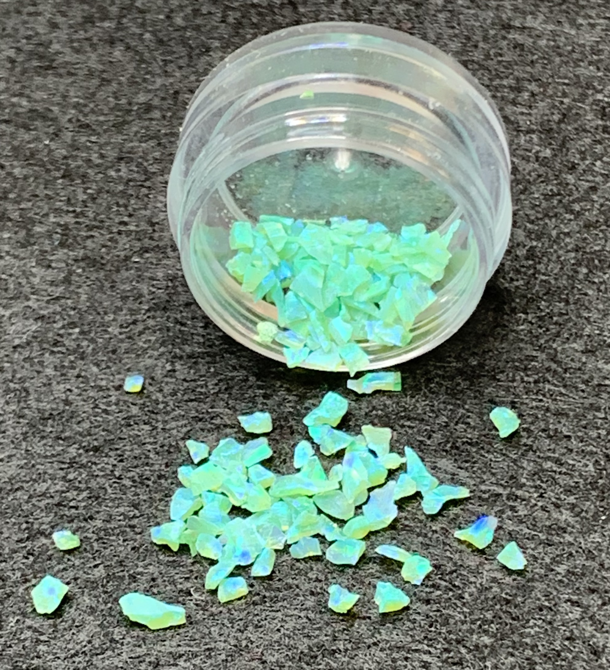 Iridescent opal flakes spilled from plastic jar