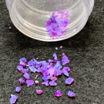 Iridescent purple glitter flakes spilling from jar